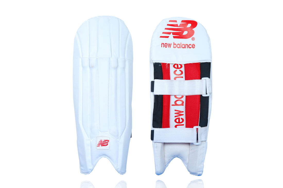 A pair of white New Balance wicket keeping pads with red accents and the brand&
