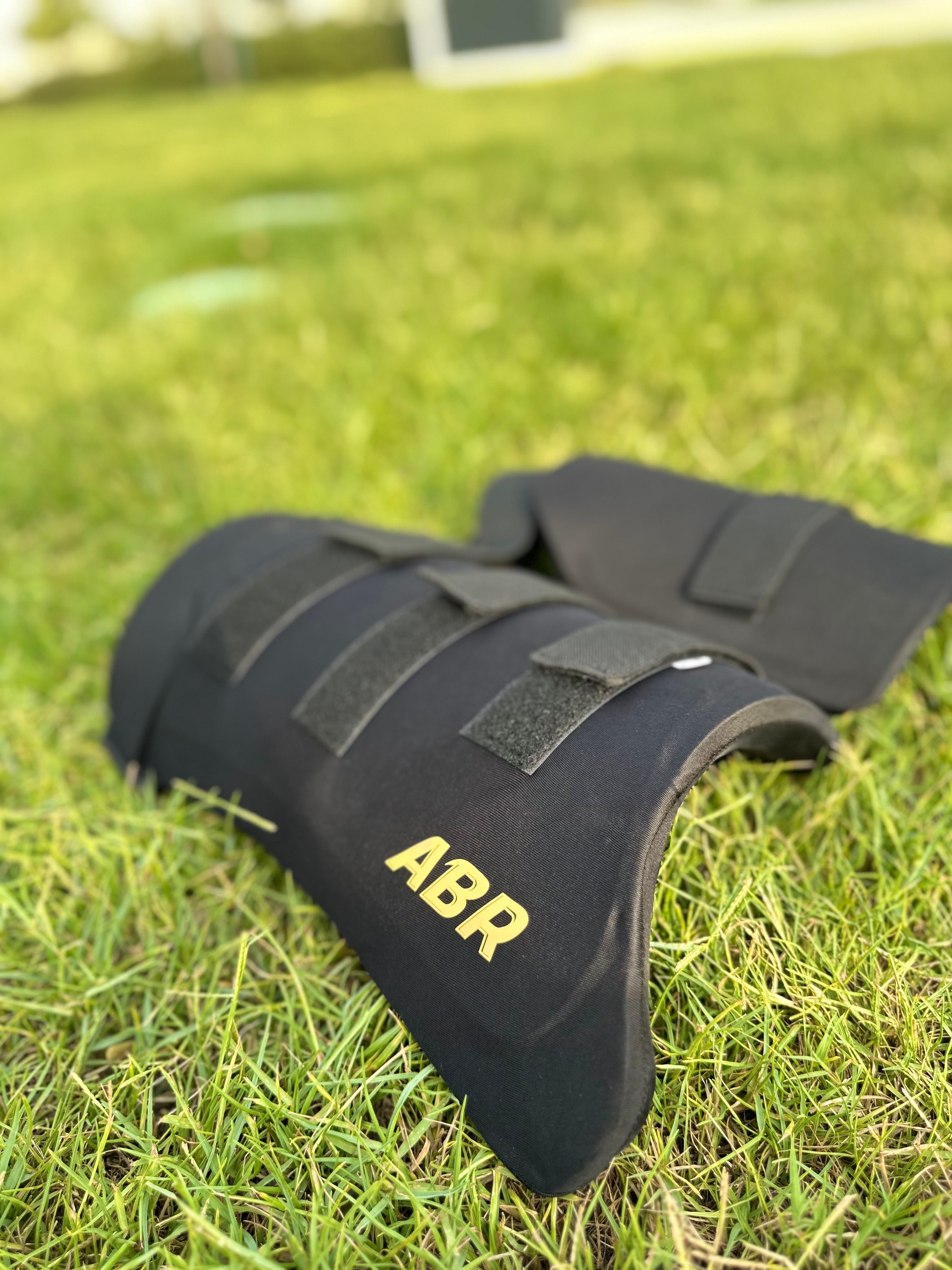 A black ABR brand thigh pad placed on grass, designed for cricket protective gear.
