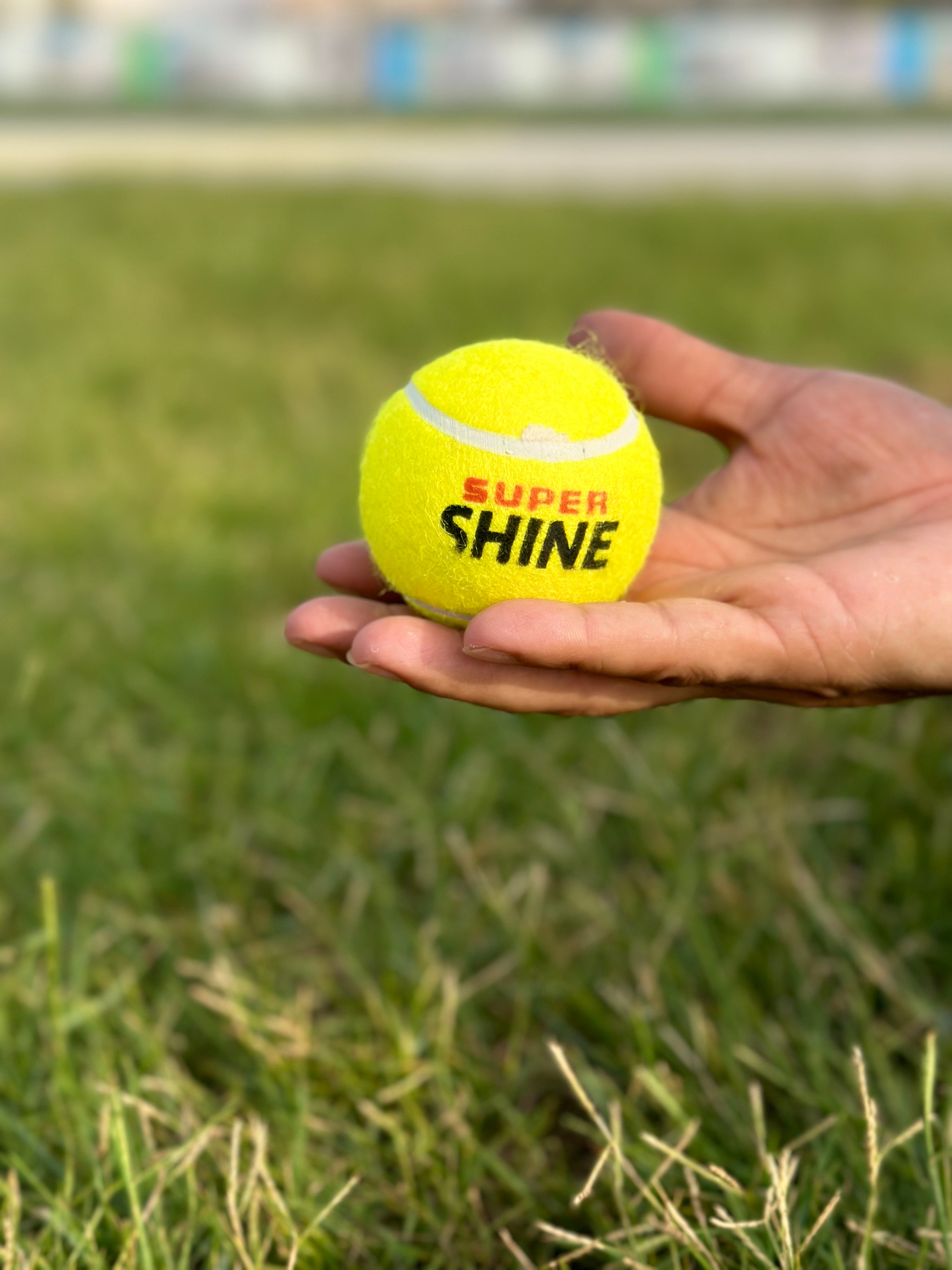 A hand holding a yellow tennis cricket ball with the text &