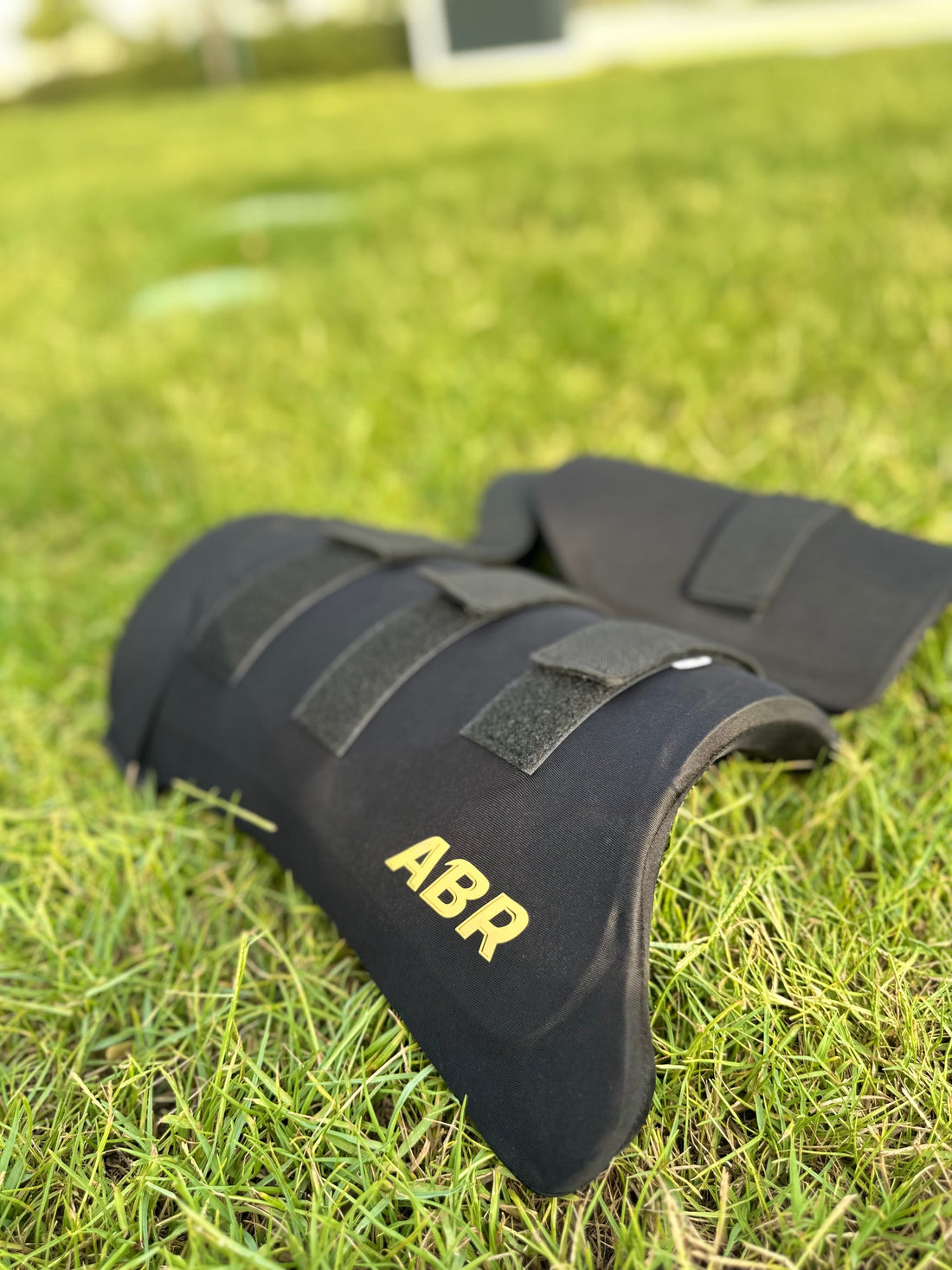 A black ABR brand thigh pad placed on grass, designed for cricket protective gear.